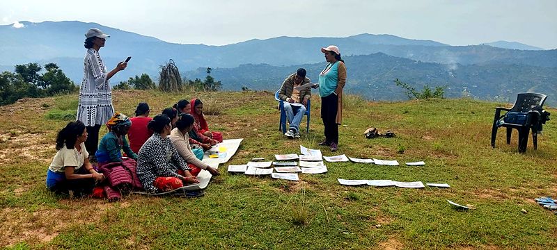 Women seated on the grass in a hillside group session with picture cards laid out on the ground